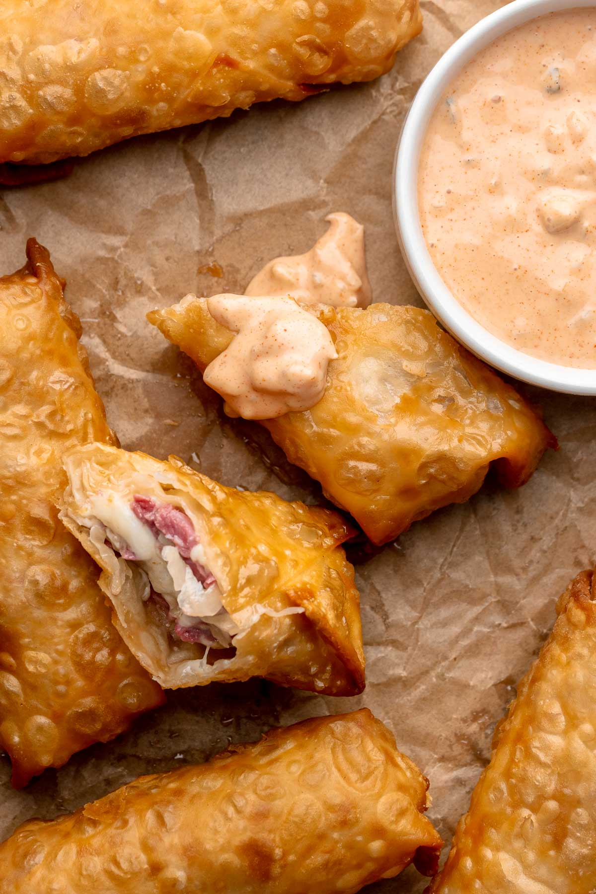 Reuben egg rolls with thousand island dip drizzled onto it.