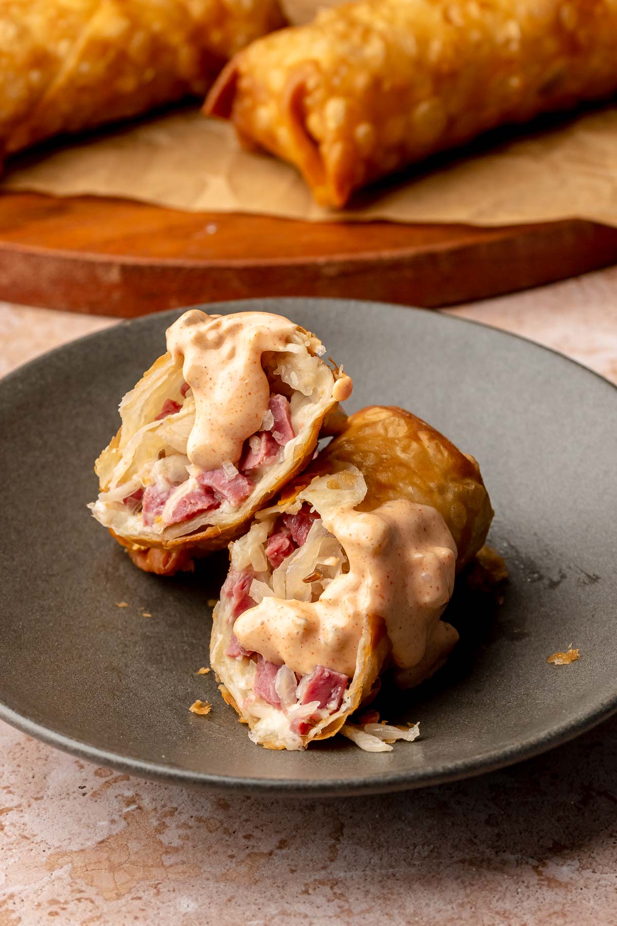 Reuben egg rolls cut on a plate with thousand island dip drizzled onto it.