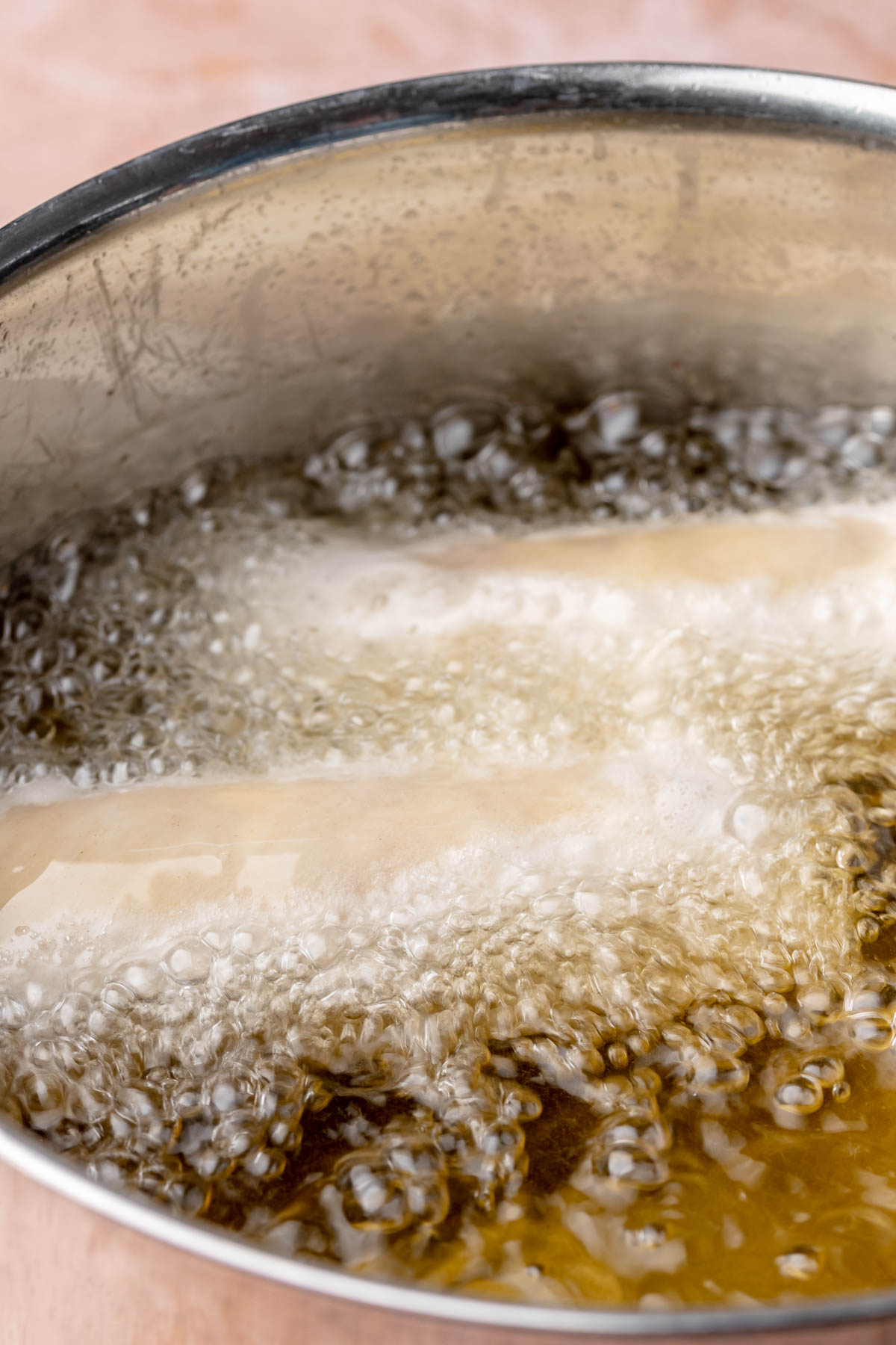 Egg rolls deep frying in bubbling oil.