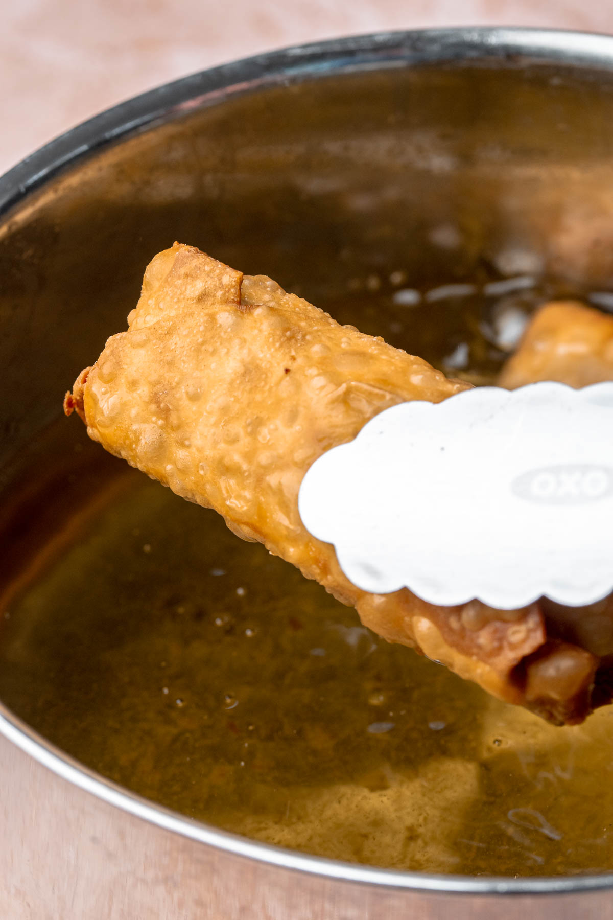 Tongs hold a fully fried, golden egg roll over hot oil.