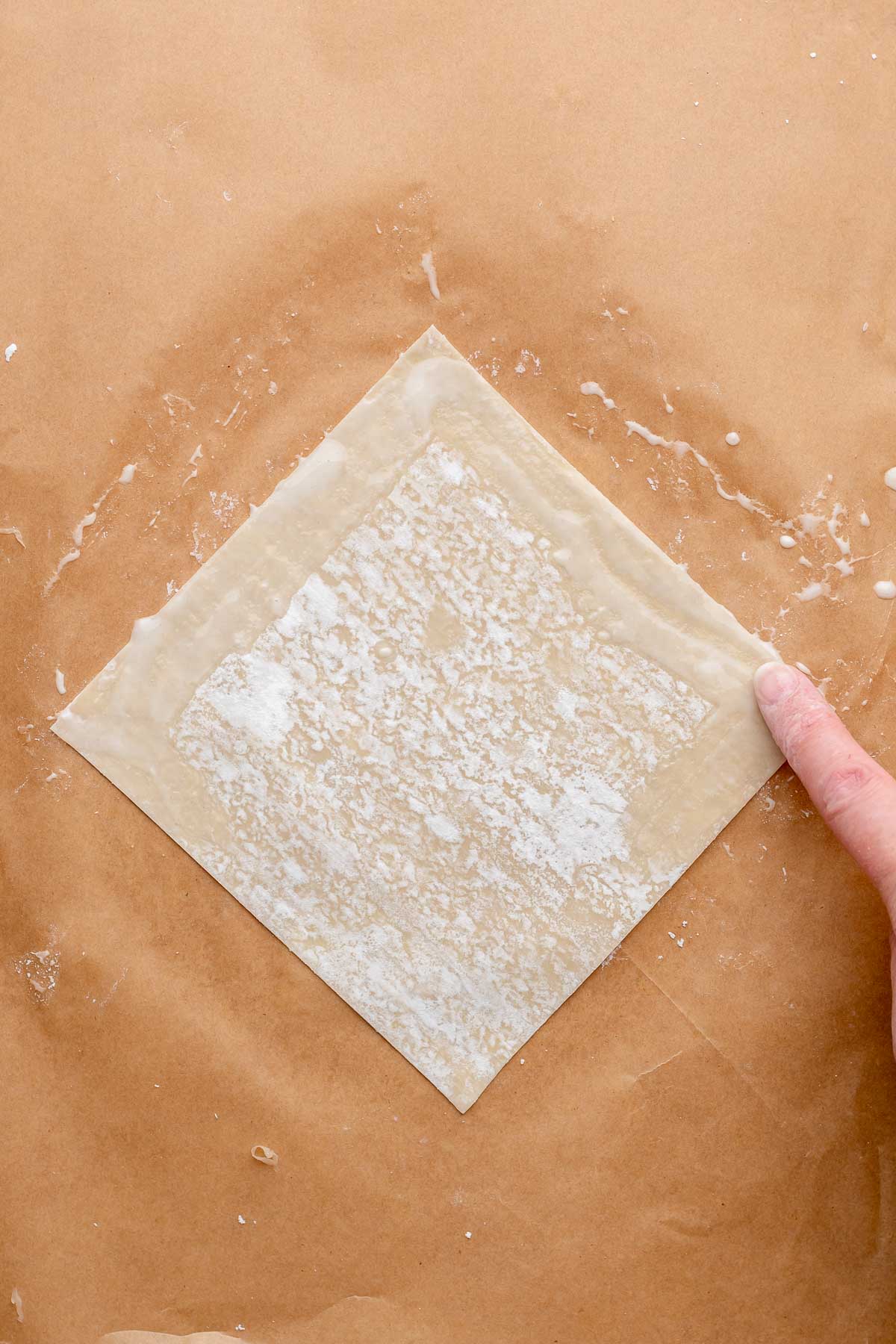 A finger swipes flour paste onto an egg roll wrapper.