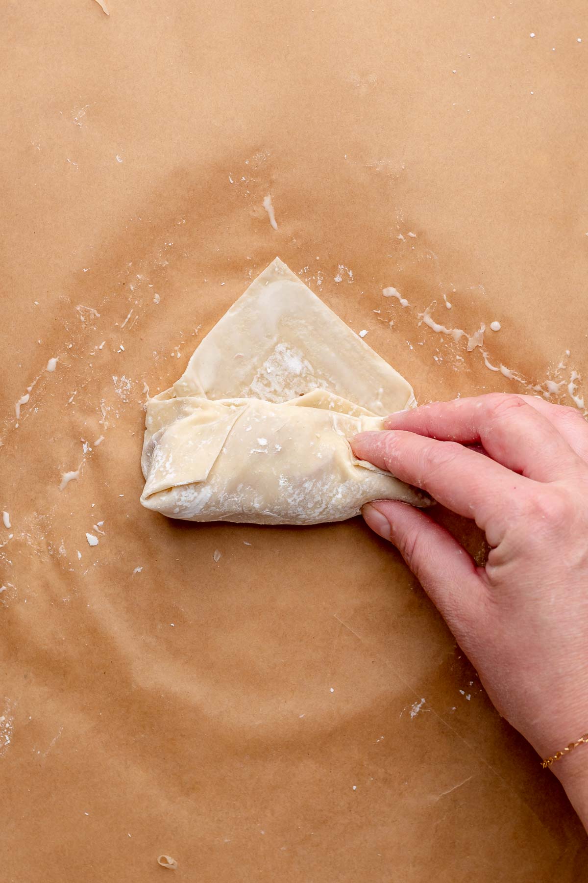 A hand folds an egg roll into shape.