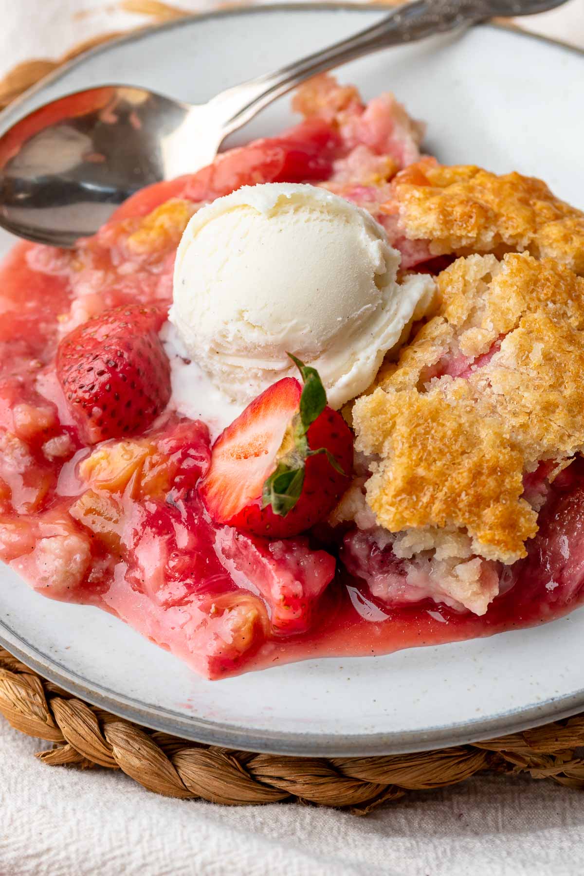 Strawberry rhubarb cobbler on a plate with a scoop of vanilla ice cream on top.