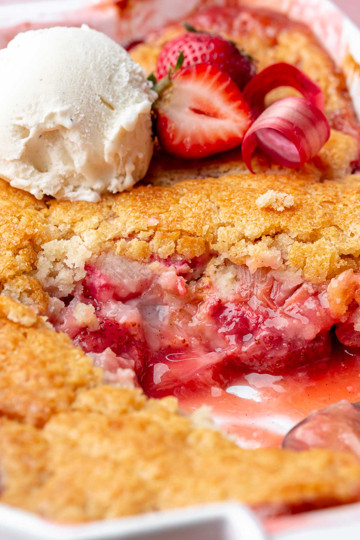 Strawberry rhubarb cobbler in a caserole dish with a scoop removed and ice cream on top.