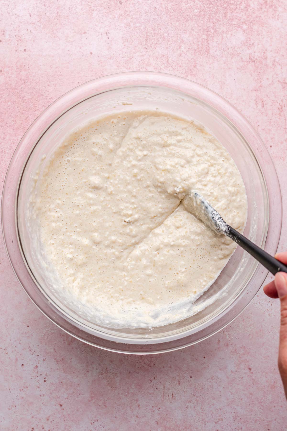 A hand mixes biquick batter with a rubber spatula.
