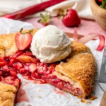 Sliced strawberry rhubarb galette with a scoop of vanilla ice cream on top.