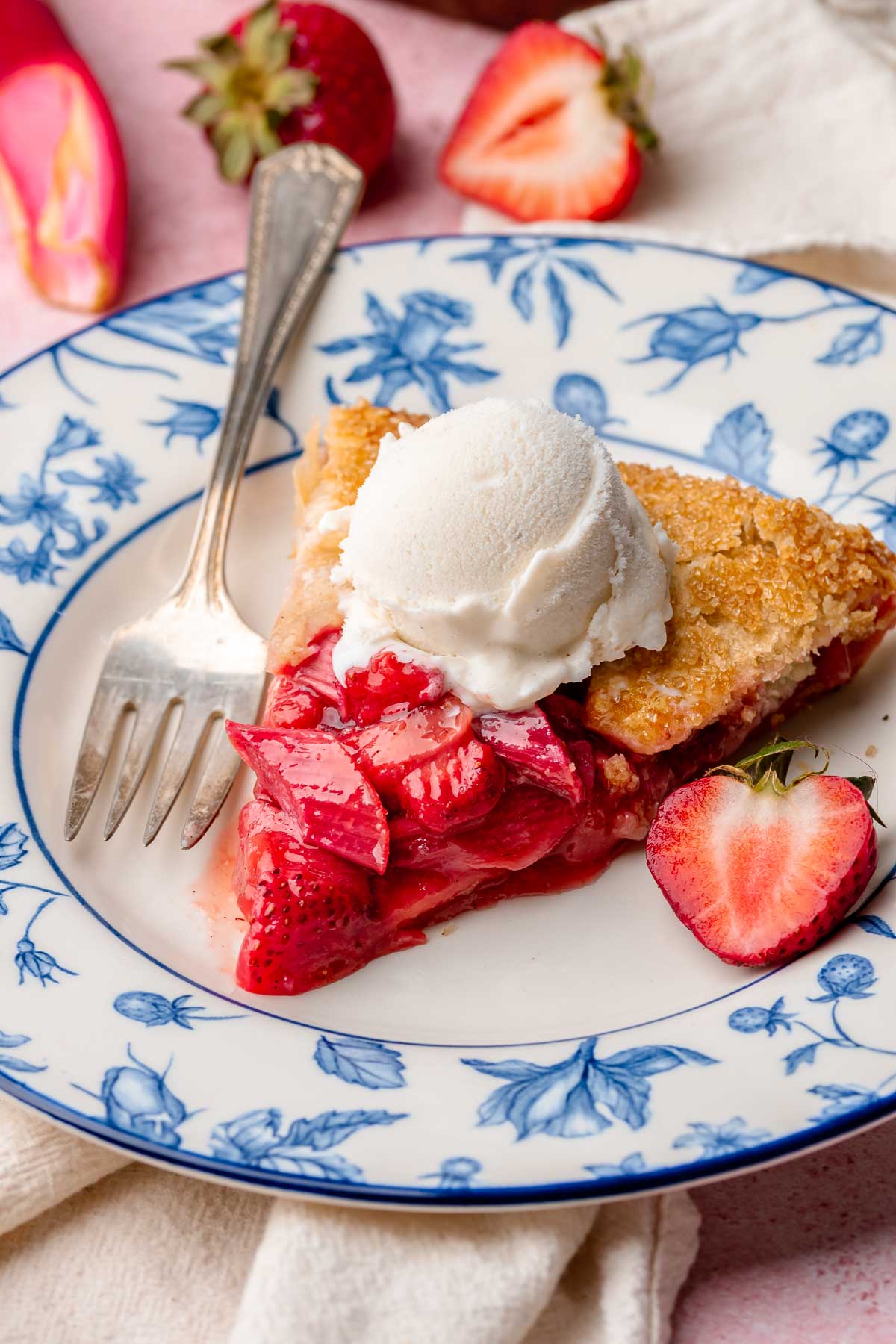 A slice of strawberry rhubarb galette on a plate with a scoop of ice cream on top and a fork on the side.