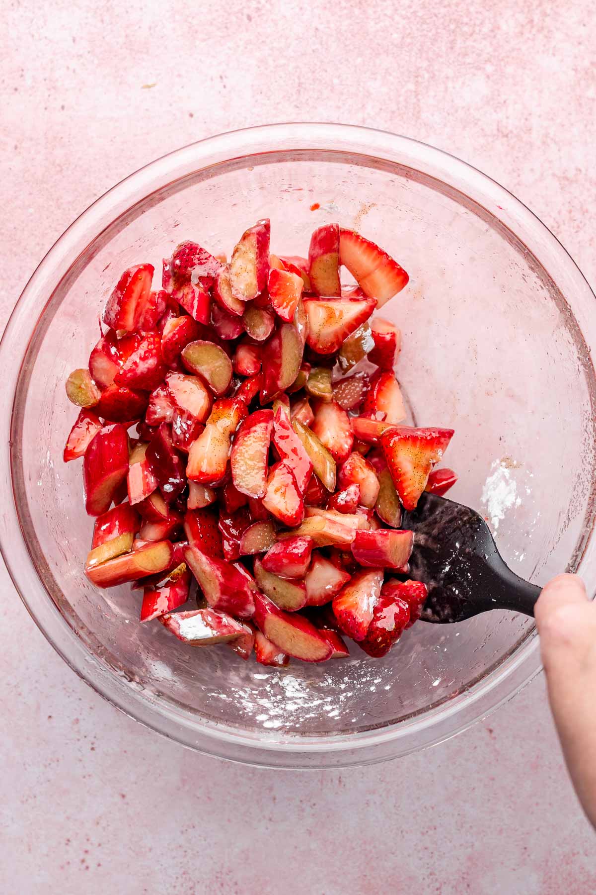 A spatula mixes strawberries and rhubarb in a bowl.