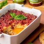 Pesto and sun dried tomato dip in a casserole dish. Some is removed.
