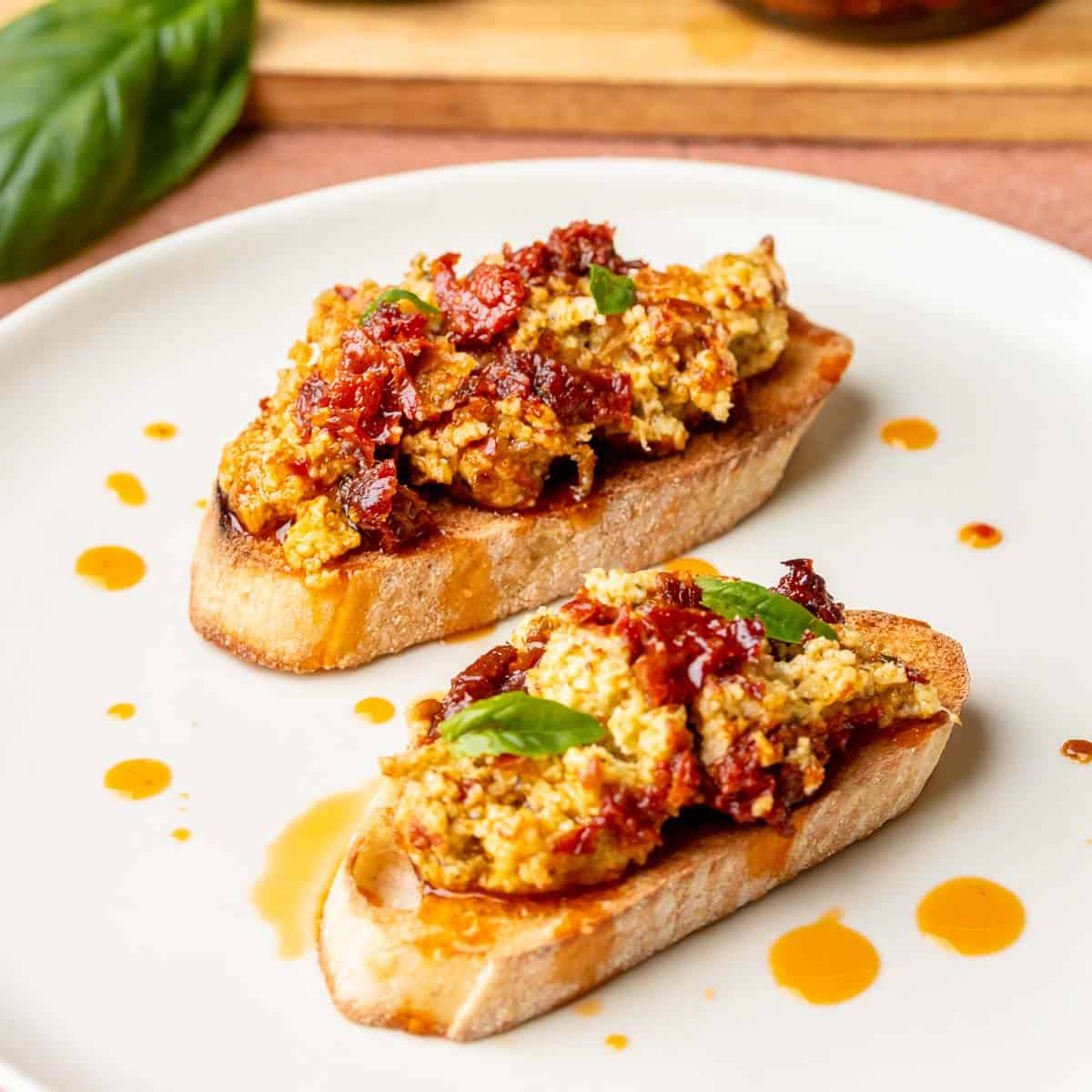 Pesto and sun dried tomato dip on crostini on a plate.