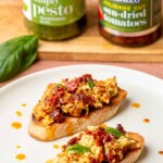 Pesto and sun dried tomato dip on crostini on a plate.