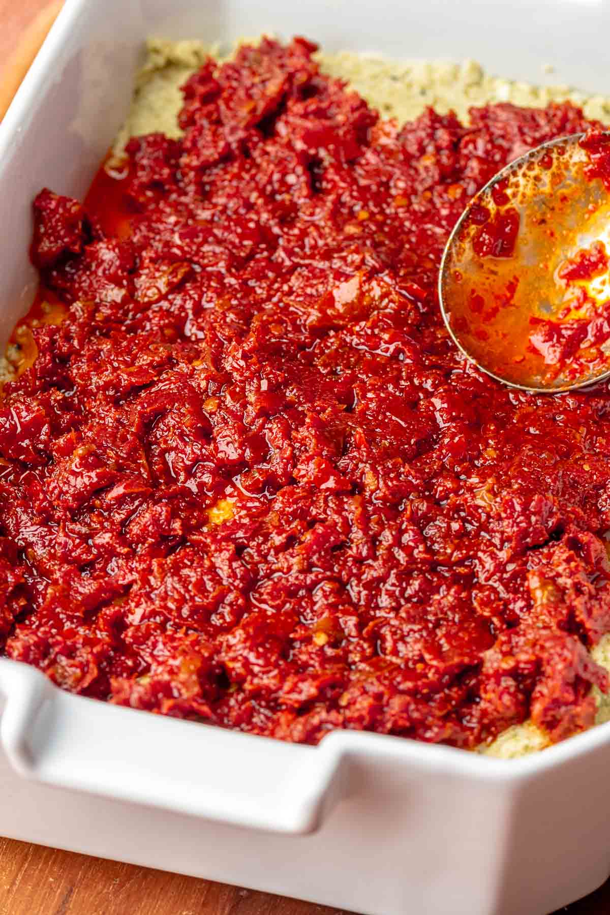 Sun-dried tomatoes being spread onto pesto dip.