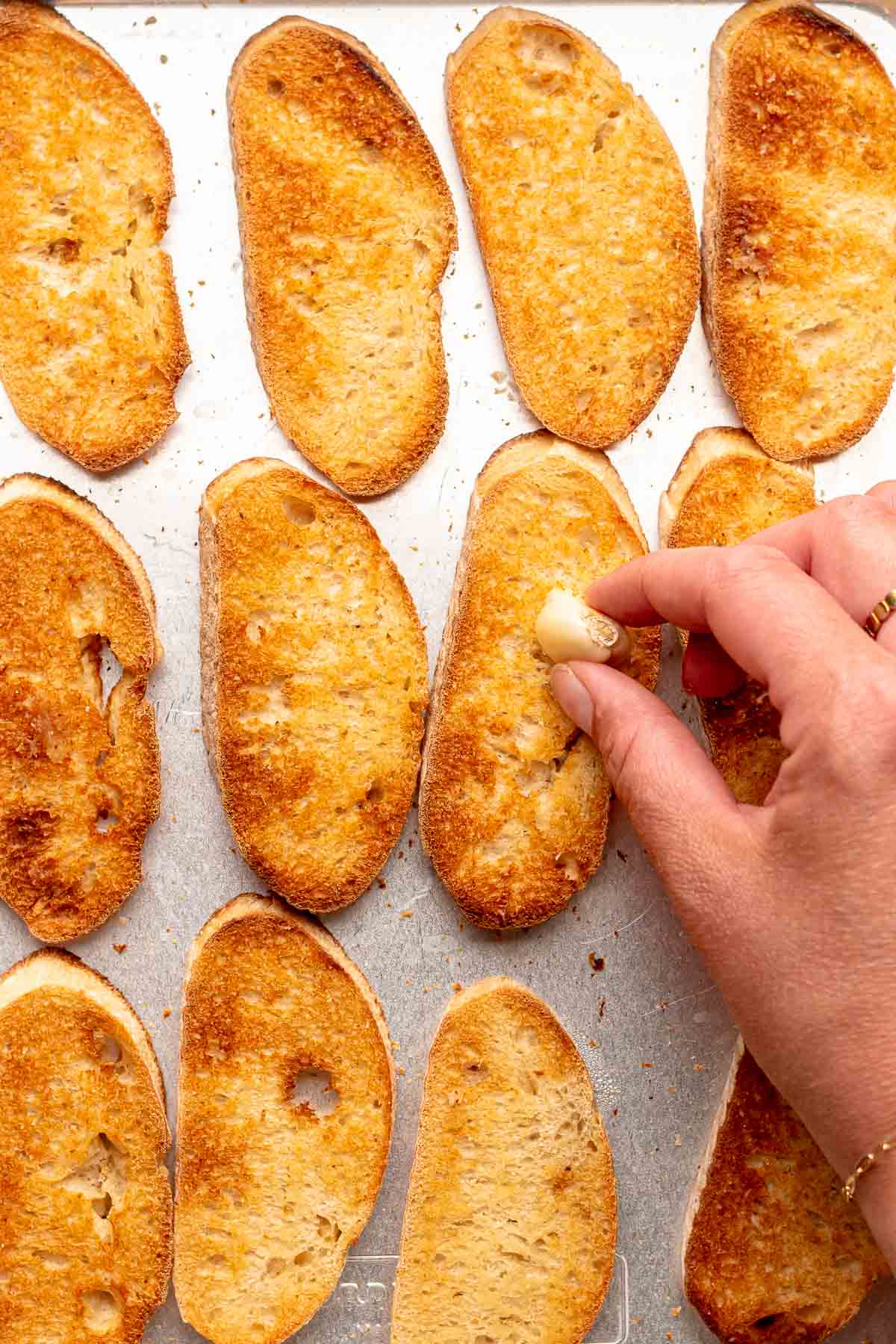 A hand rubs a piece of garlic onto toasted bread slices.