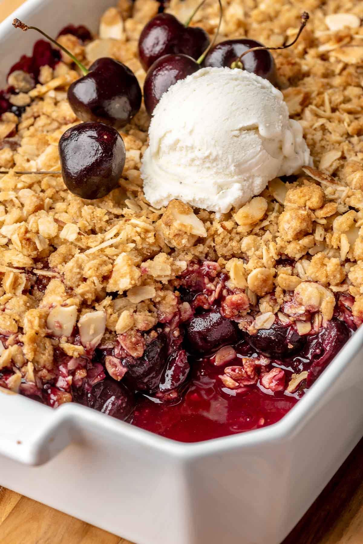 Cherry crisp in a casserole dish with a spoonful removed and a scoop of ice cream on top.