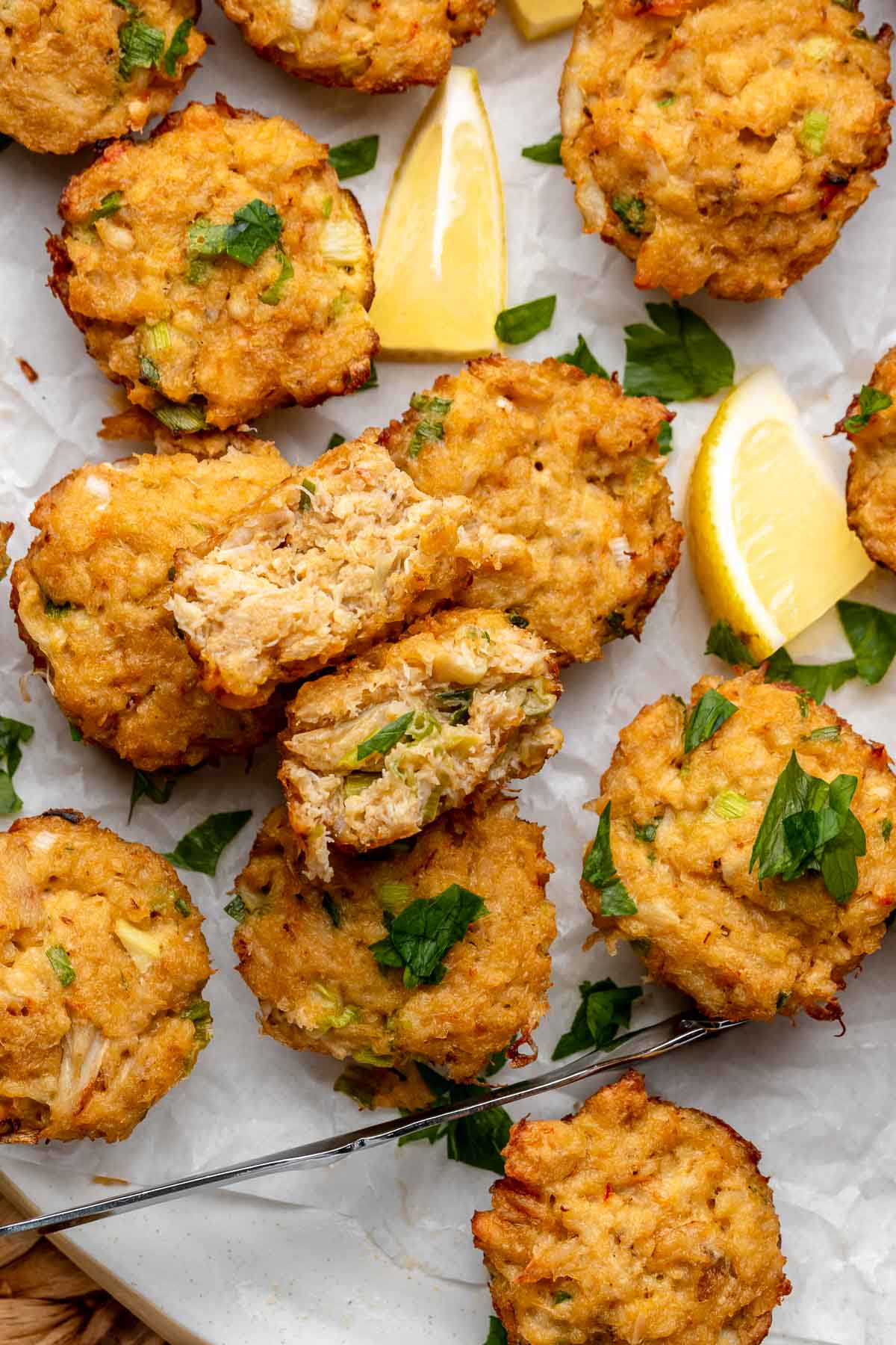 Mini crab cakes scattered on a platter with parsley and lemon wedges.