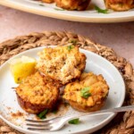 Three mini crab cakes on a plate. One crab cake is half eaten.