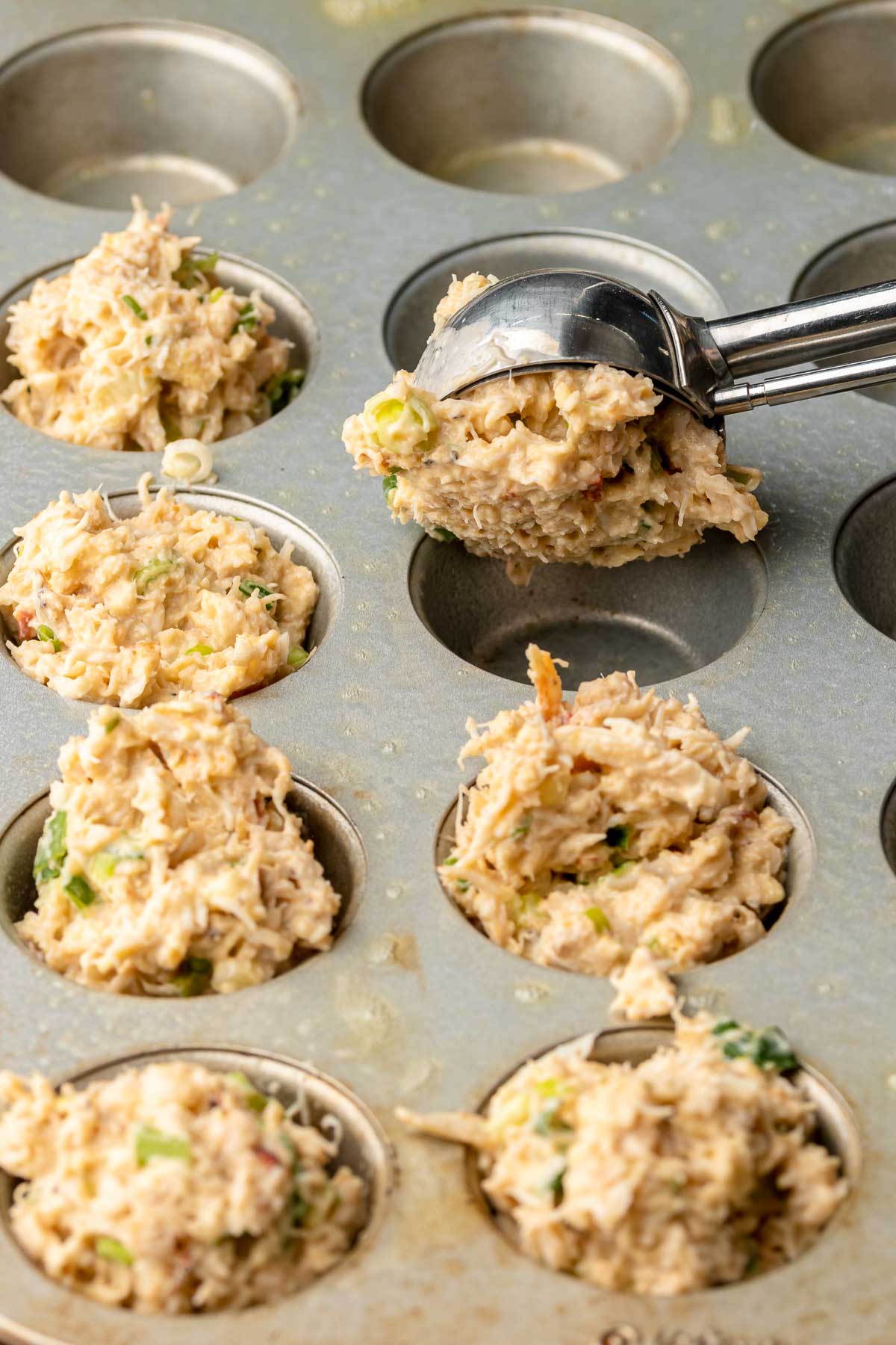 A trigger scoop adds crab cake batter into a mini muffin tin well.