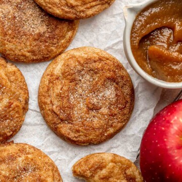 Apple butter cookies on parchment paper with apple butter and an apple on the side.