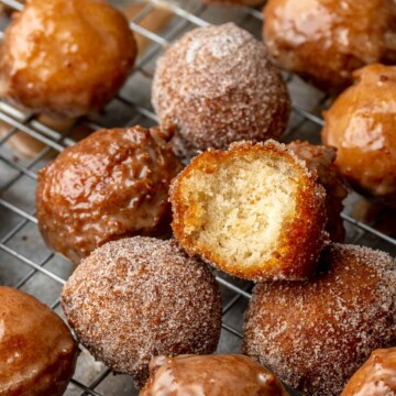 Apple cider donut holes on a wire rack. One has a bite removed.