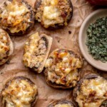 Sausage apple stuffed mushrooms on parchment paper. One is cut in half to show the insides.