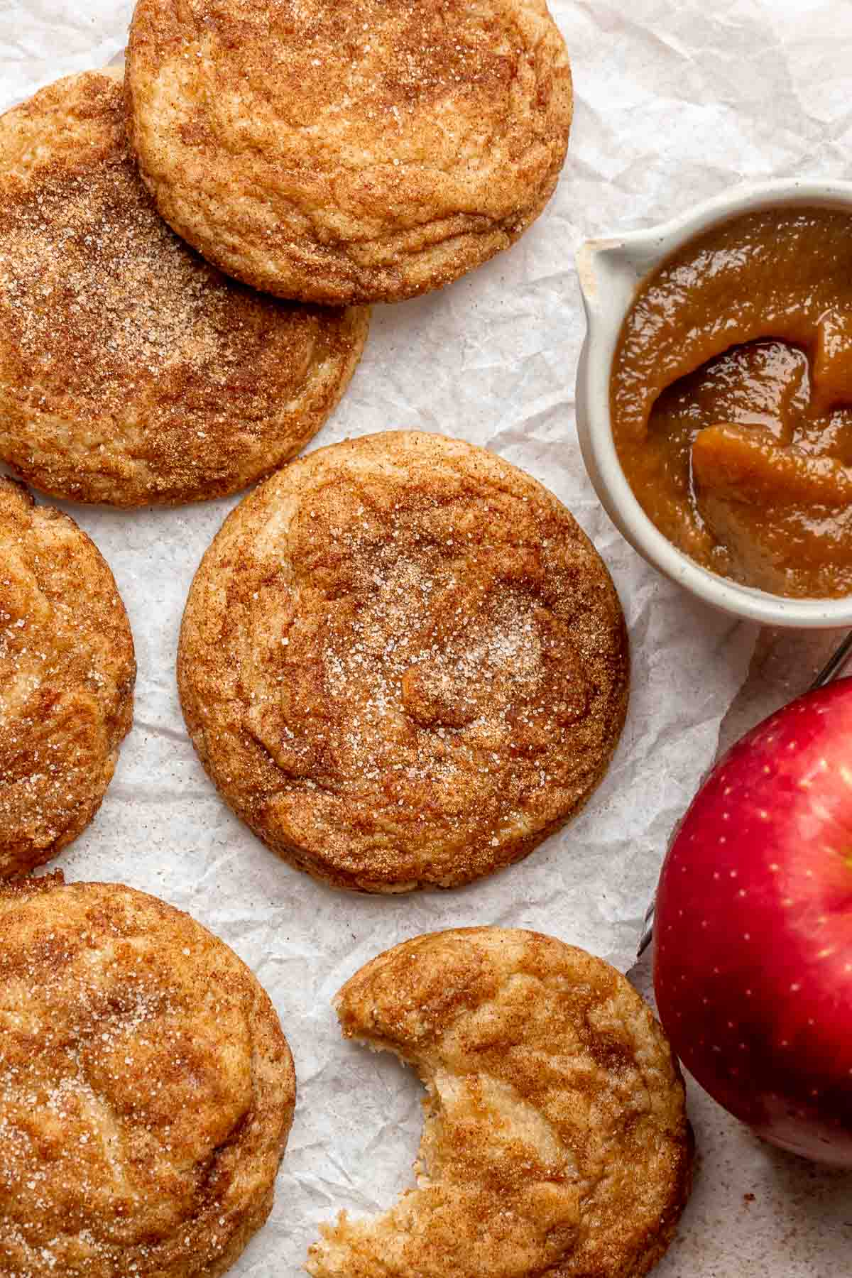 Apple butter cookies on parchment paper with apple butter and an apple on the side.