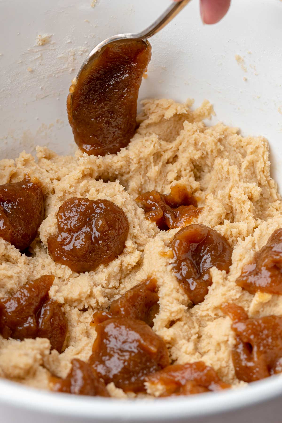 A spoon adds dollops of apple butter into the cookie dough.