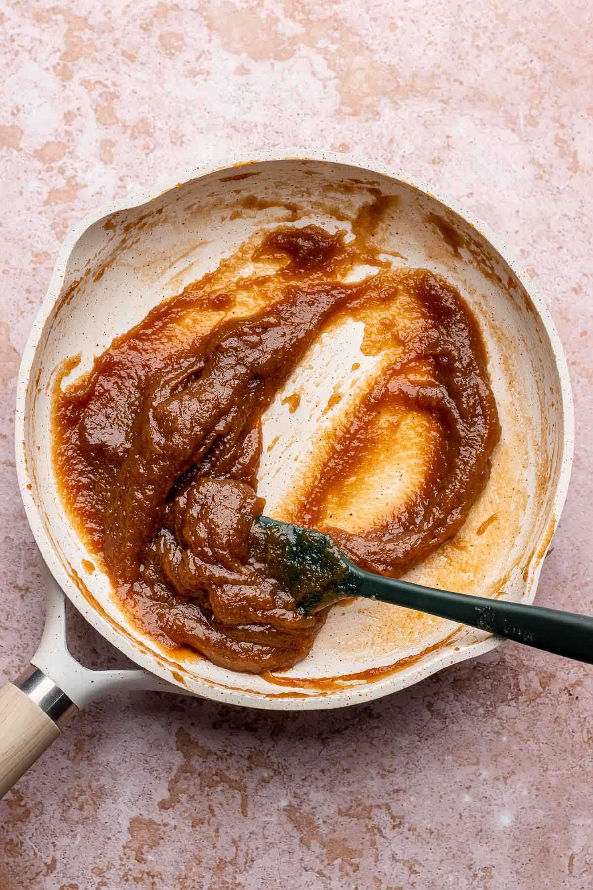 A spatula mixes apple butter in a frying pan.