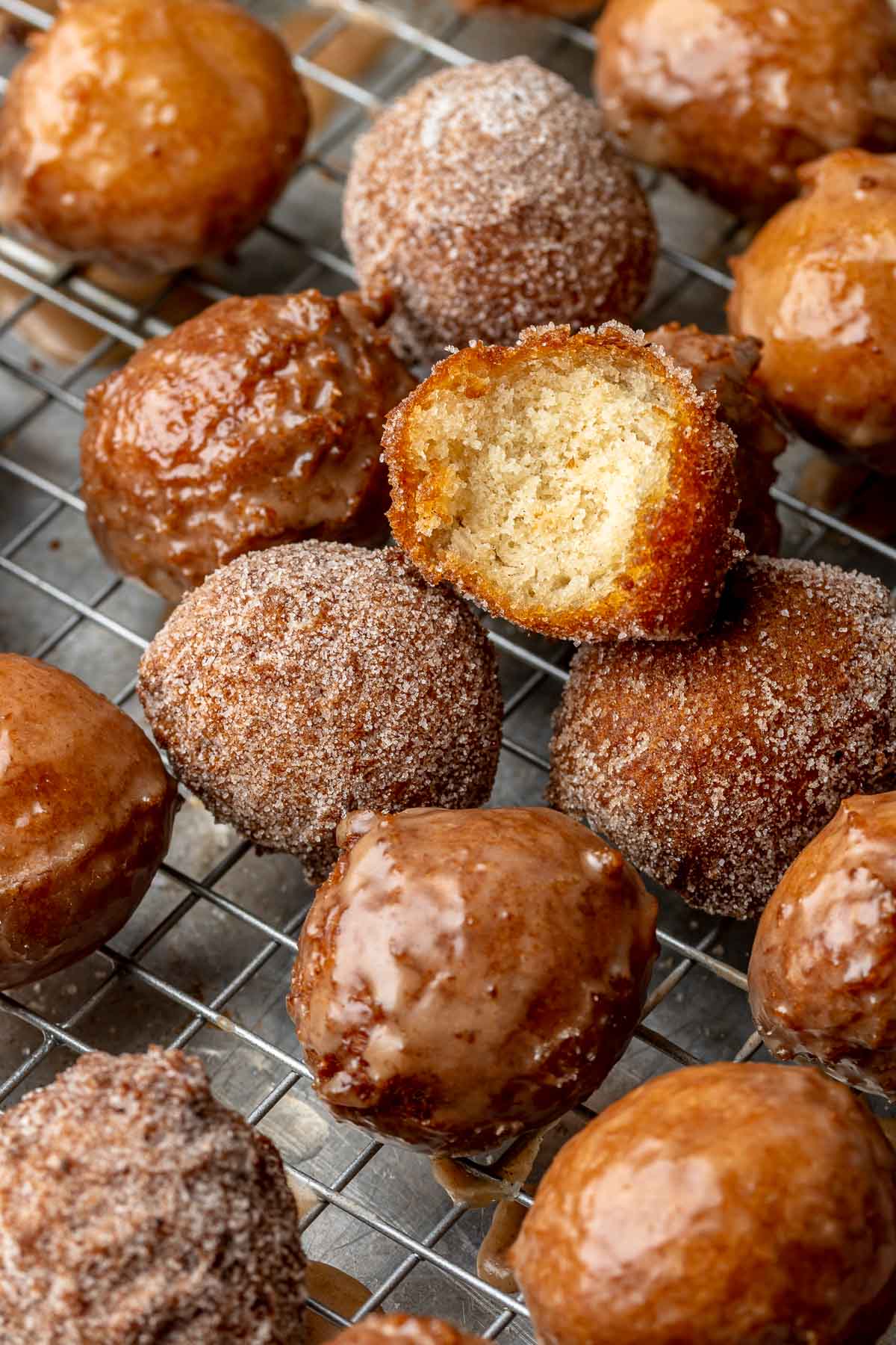 Apple cider donut holes on a wire rack. One has a bite removed.