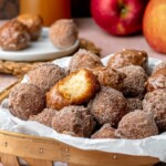 Apple cider donut holes in a basket. One has a bite removed.