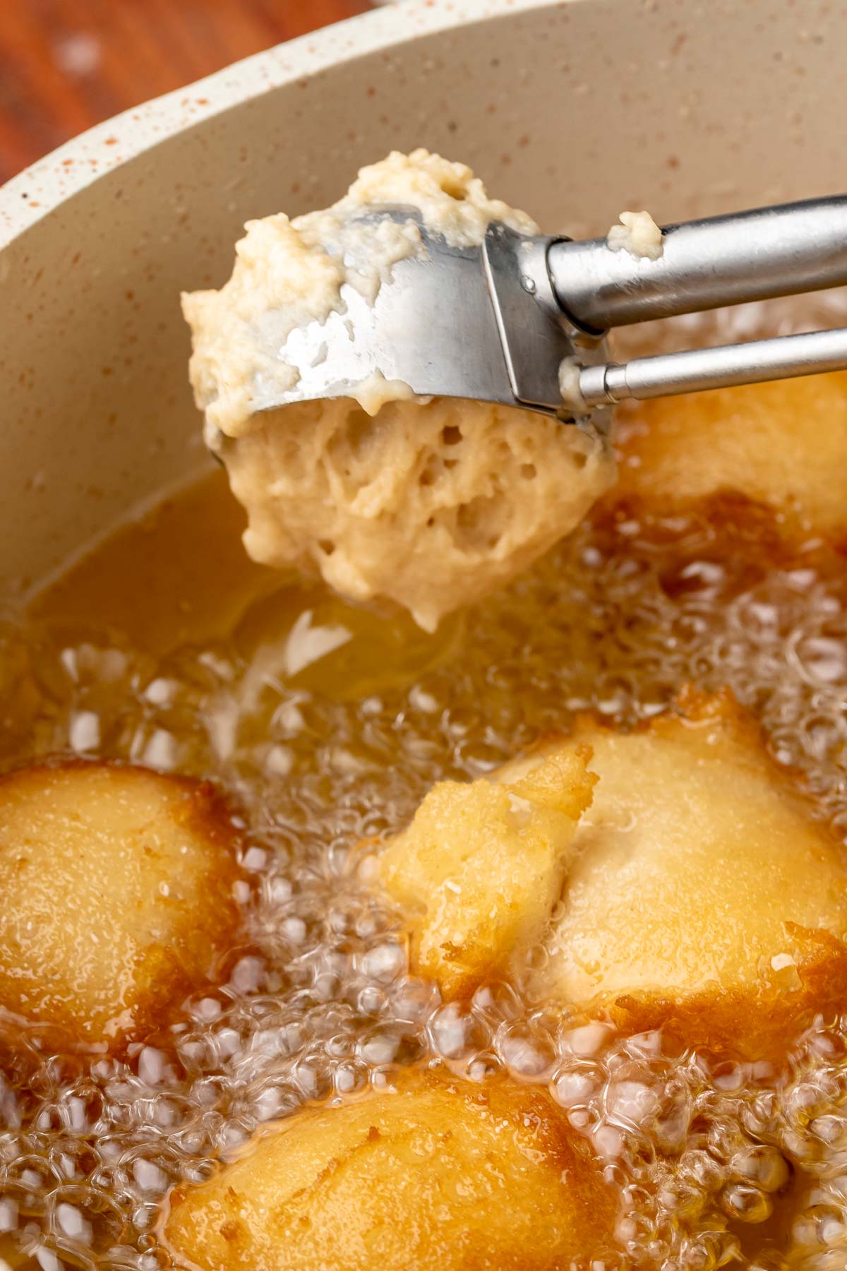 A cookie scoop drops donut batter into hot oil.