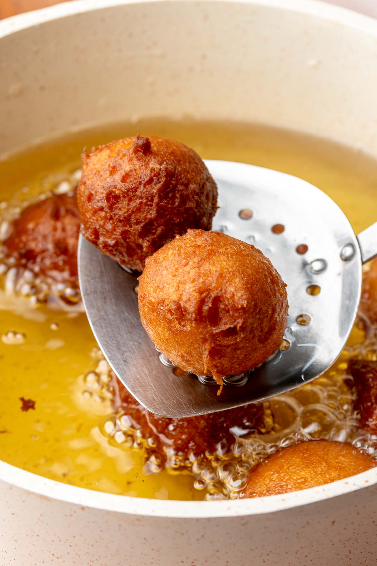 Golden fried donuts on a metal slotted spoon over frying oil.