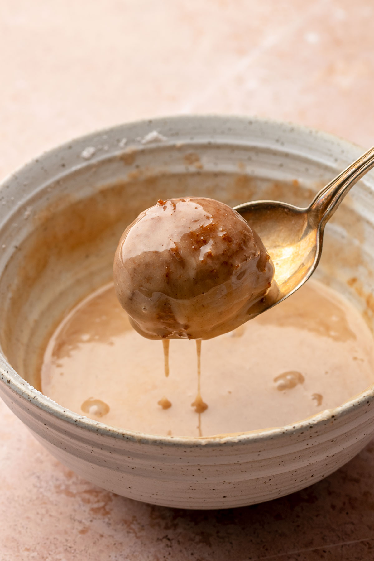 A spoon holds an apple cider donut in the bowl of glaze.