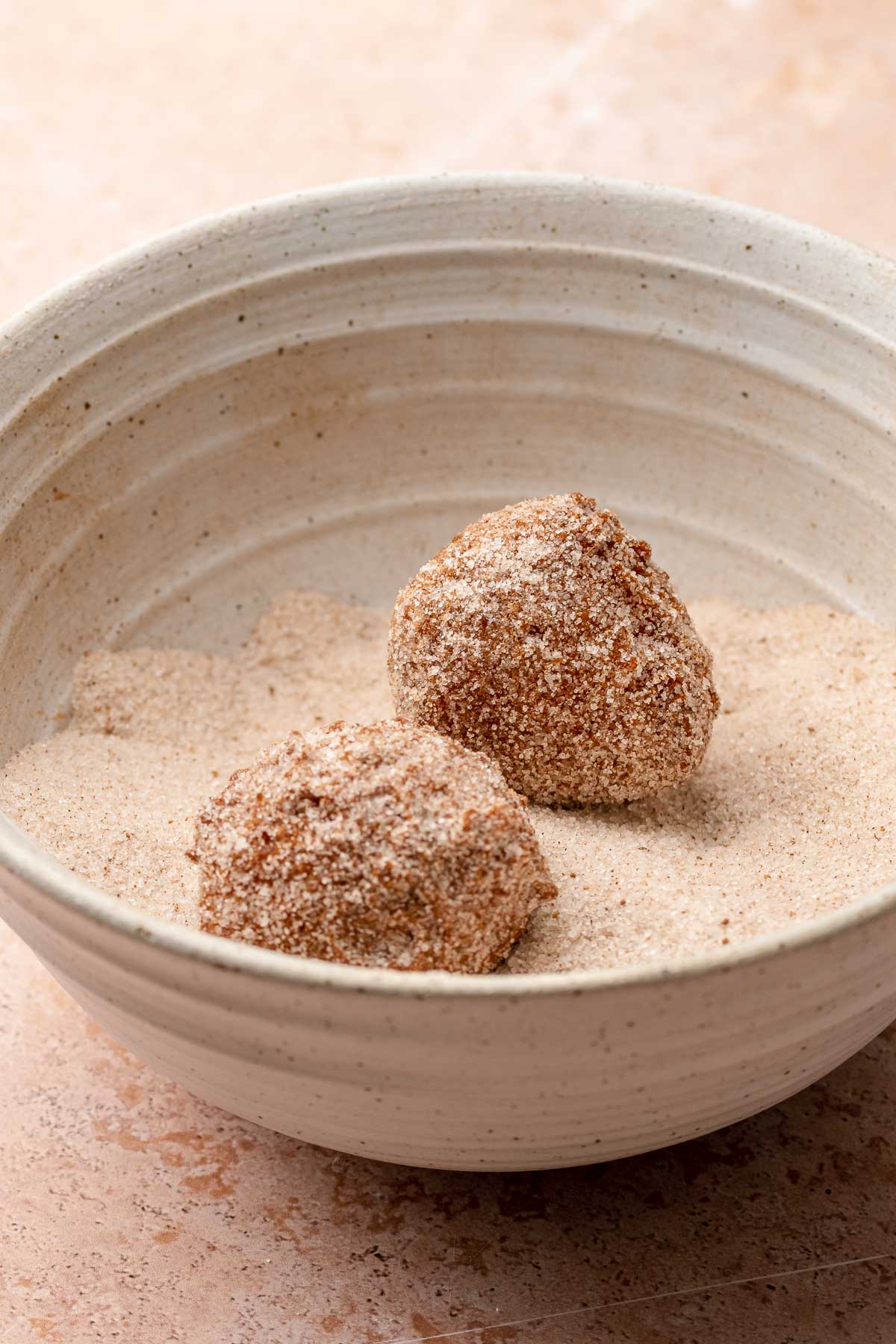 Two donut holes in a bowl of spiced sugar.