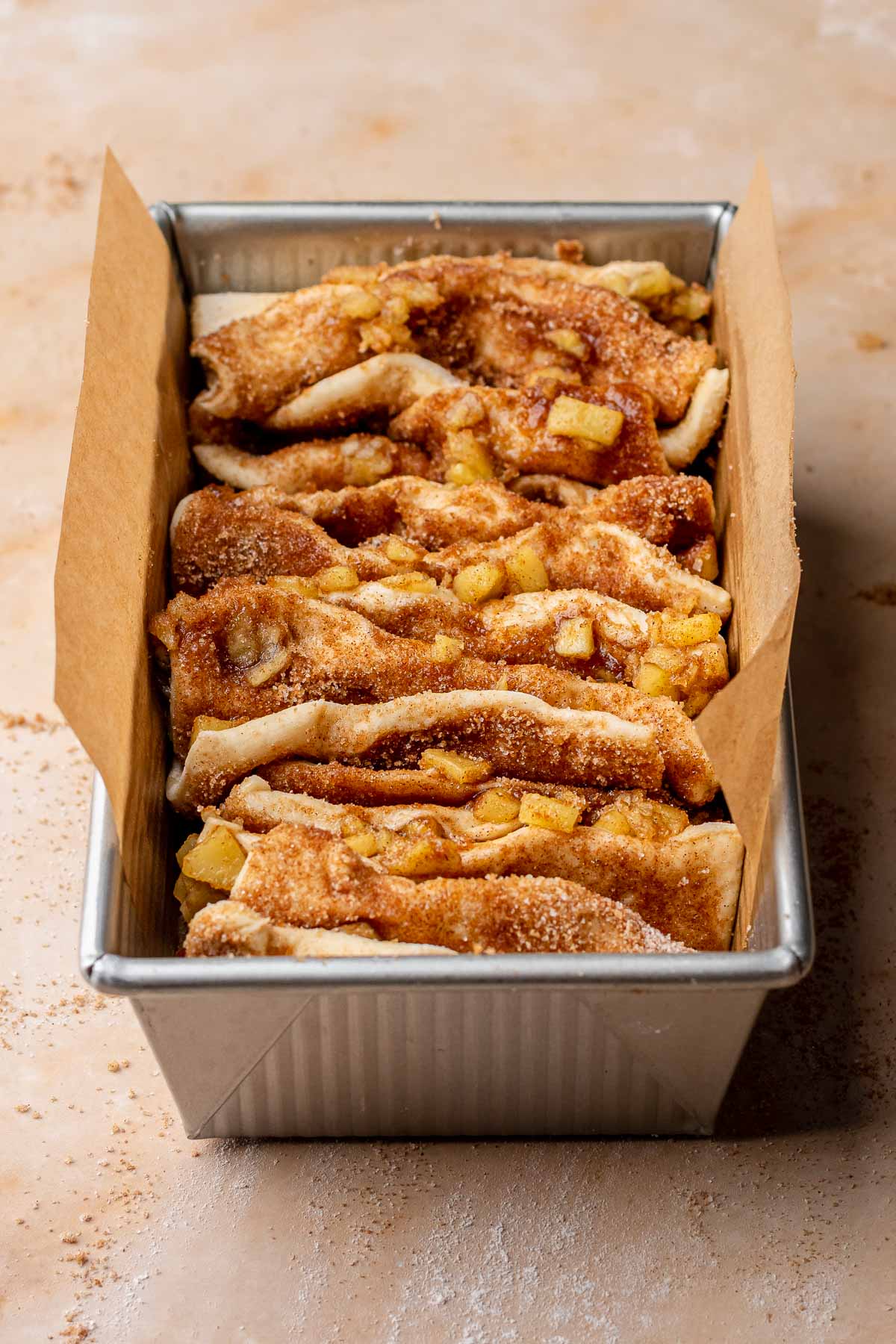 Apple fritter pull apart bread dough in a parchment lined loaf pan.
