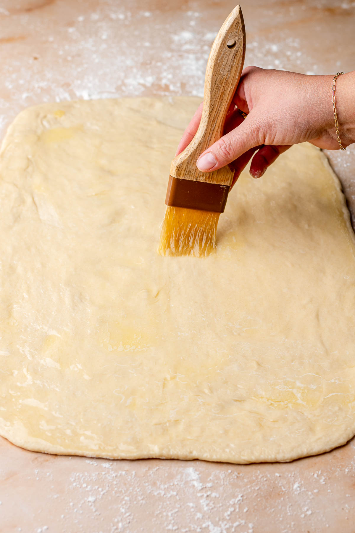 A hand brushes melted butter on a rectangle of rolled dough.