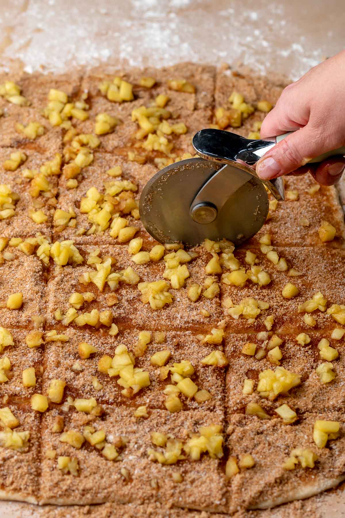 A hand cuts the apple fritter dough with a pizza wheel.