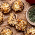 Sausage apple stuffed mushrooms on parchment paper. One is cut in half to show the insides.