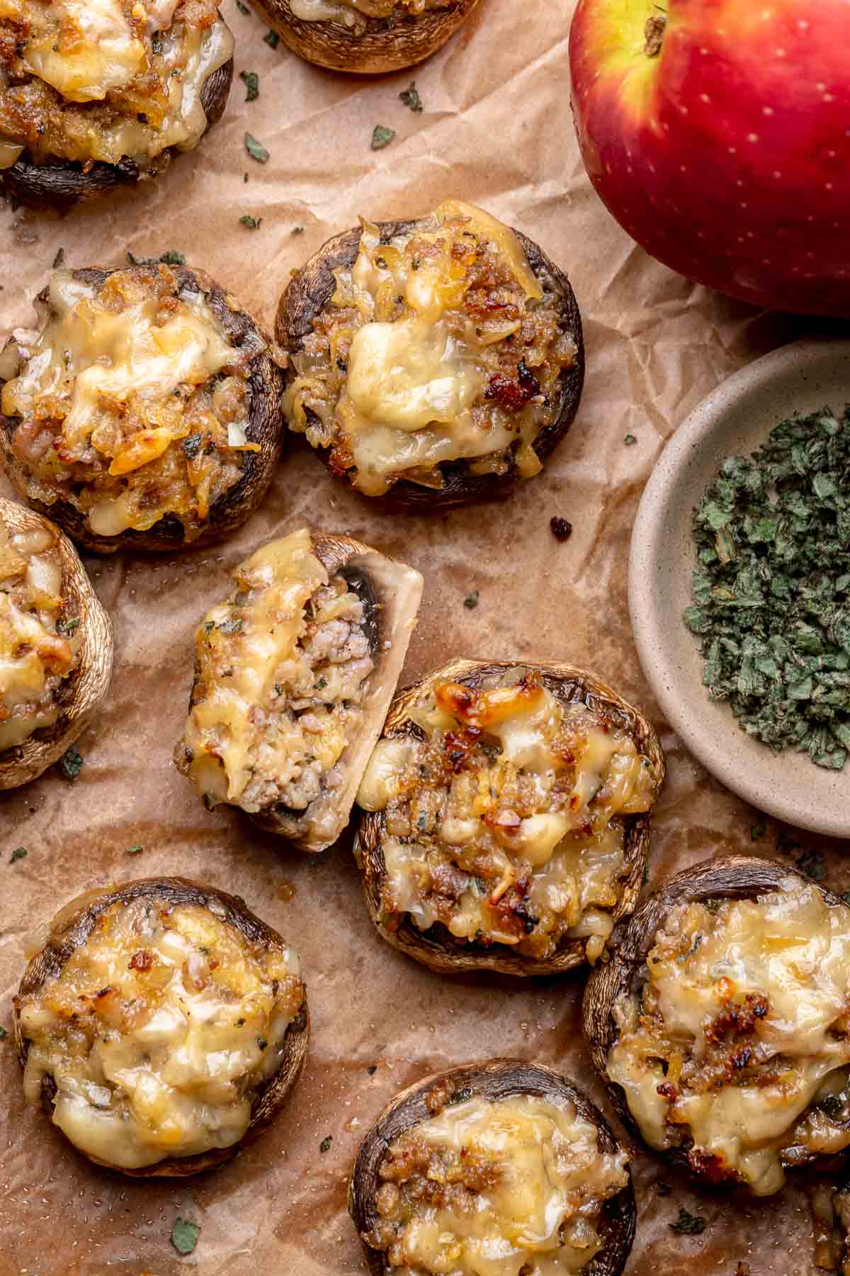 Sausage apple stuffed mushrooms on parchment paper. One is cut in half to show the insides.