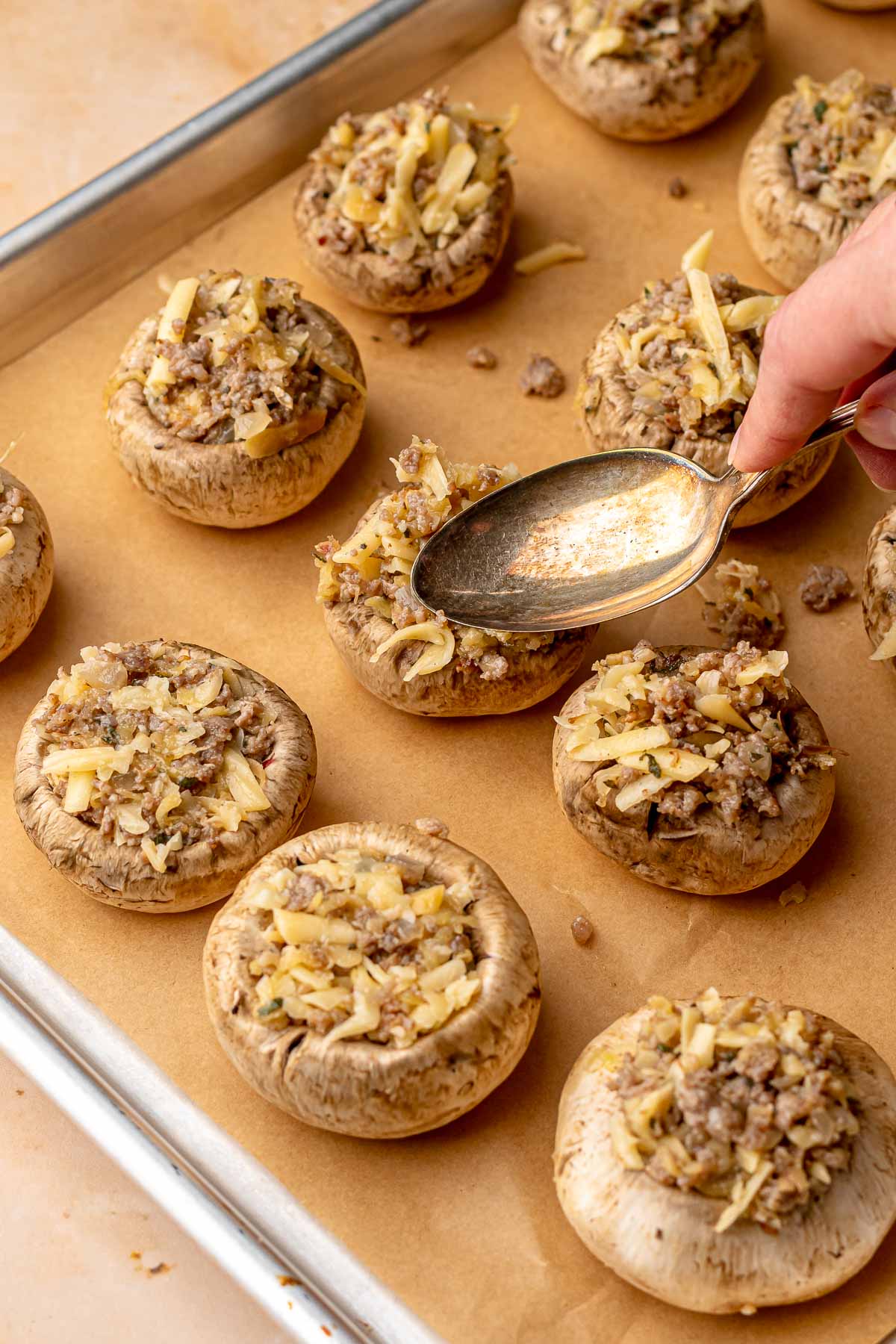 A spoon pushes filling into a mushroom cap on a pan.