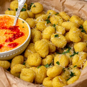 Air fryer gnocchi in a basket with a bowl of dipping sauce.