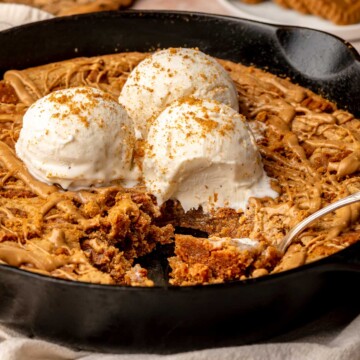 Skillet cookie with ice cream on top and spoons laying inside with pieces removed.