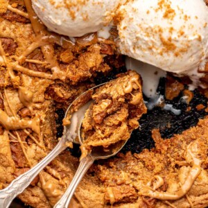 Skillet cookie with ice cream on top and spoons laying inside with pieces removed.