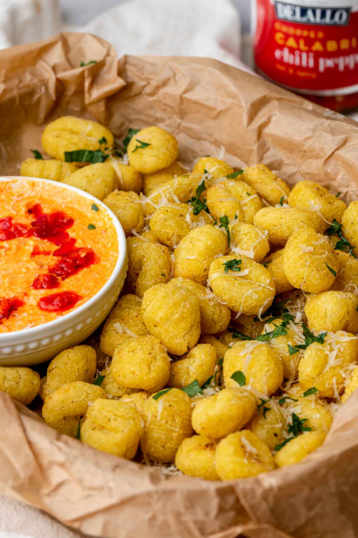 Air fryer gnocchi in a basket with a bowl of dipping sauce.