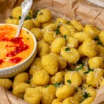 Air fryer gnocchi in a basket with a bowl of dipping sauce.