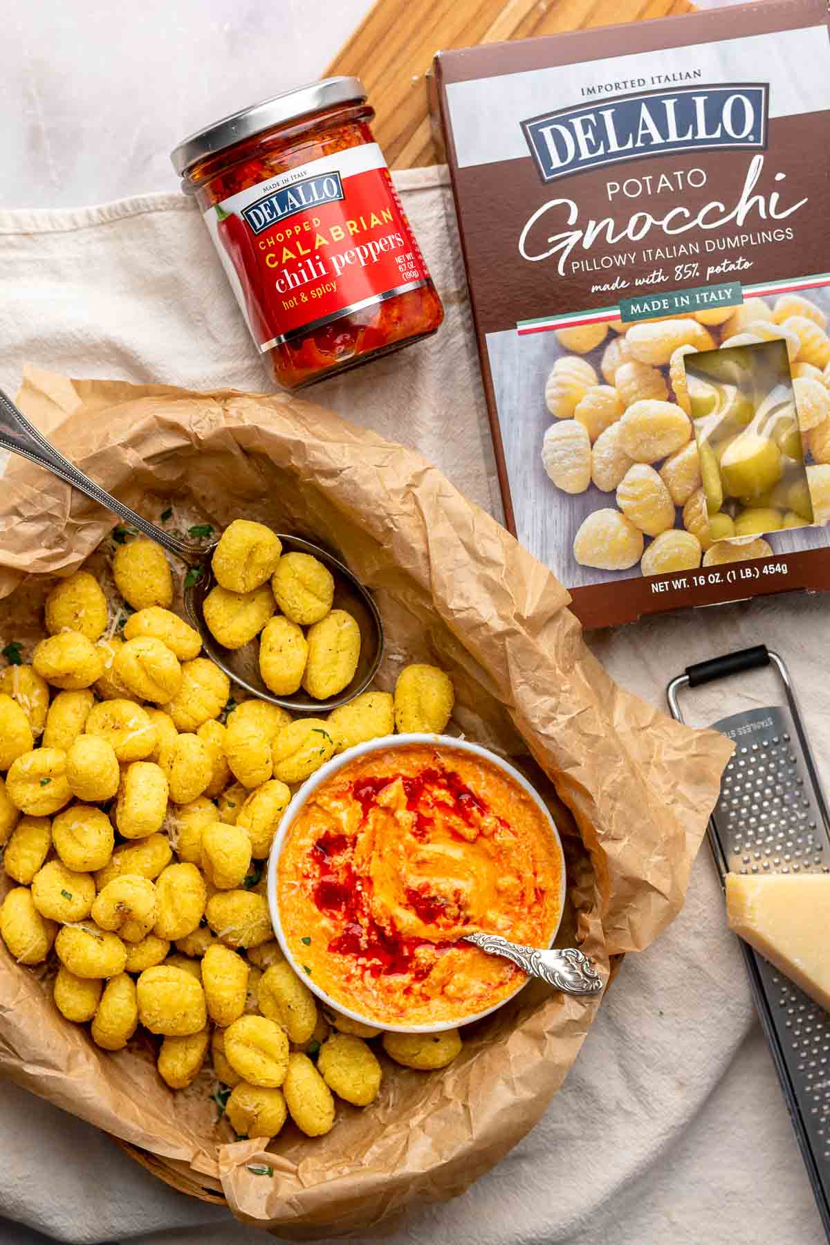 Air fryer gnocchi in a basket with a bowl of dipping sauce. The ingredients are in the background.