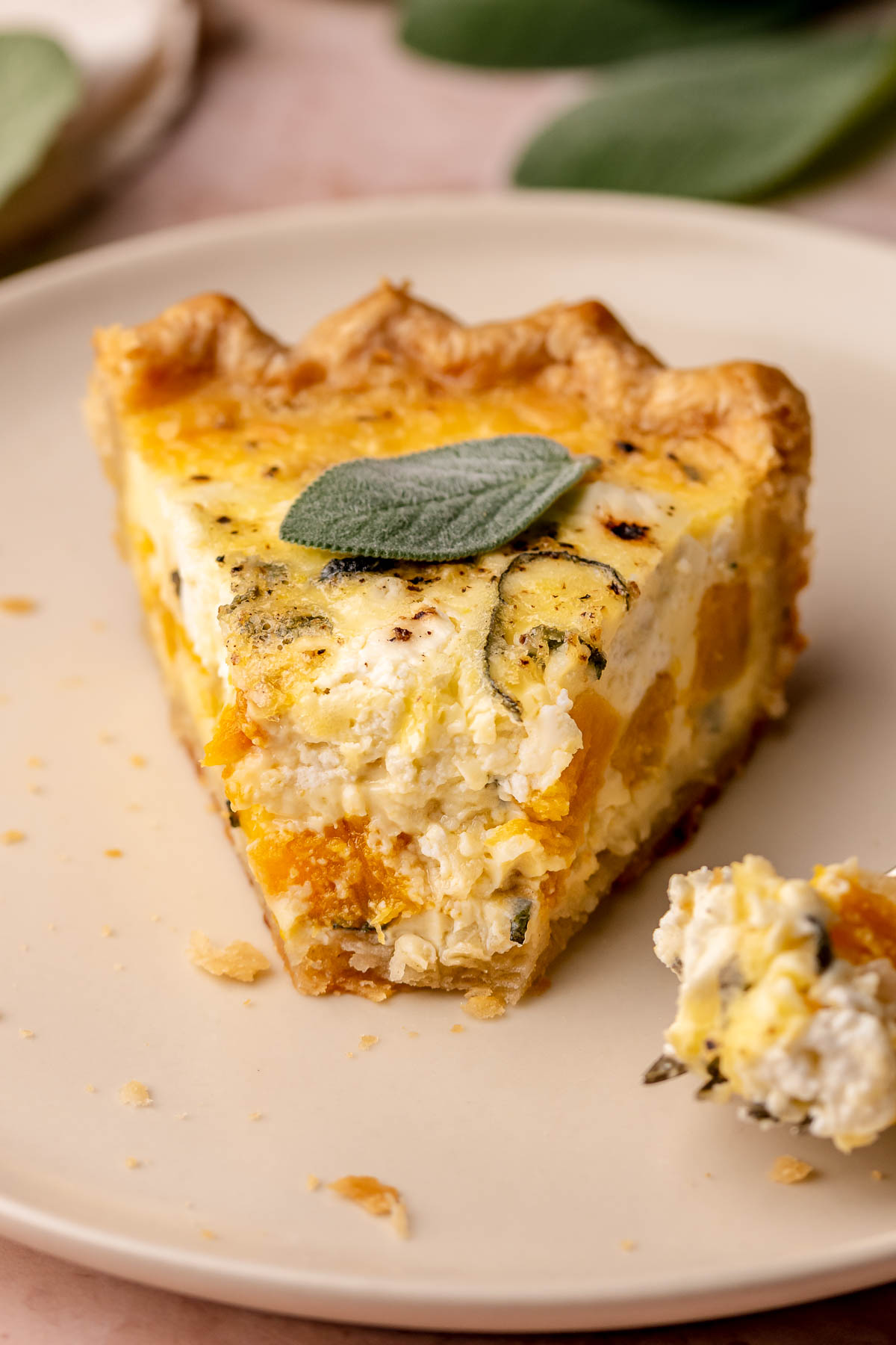 Slice of butternut squash quiche on a plate with a bite removed.