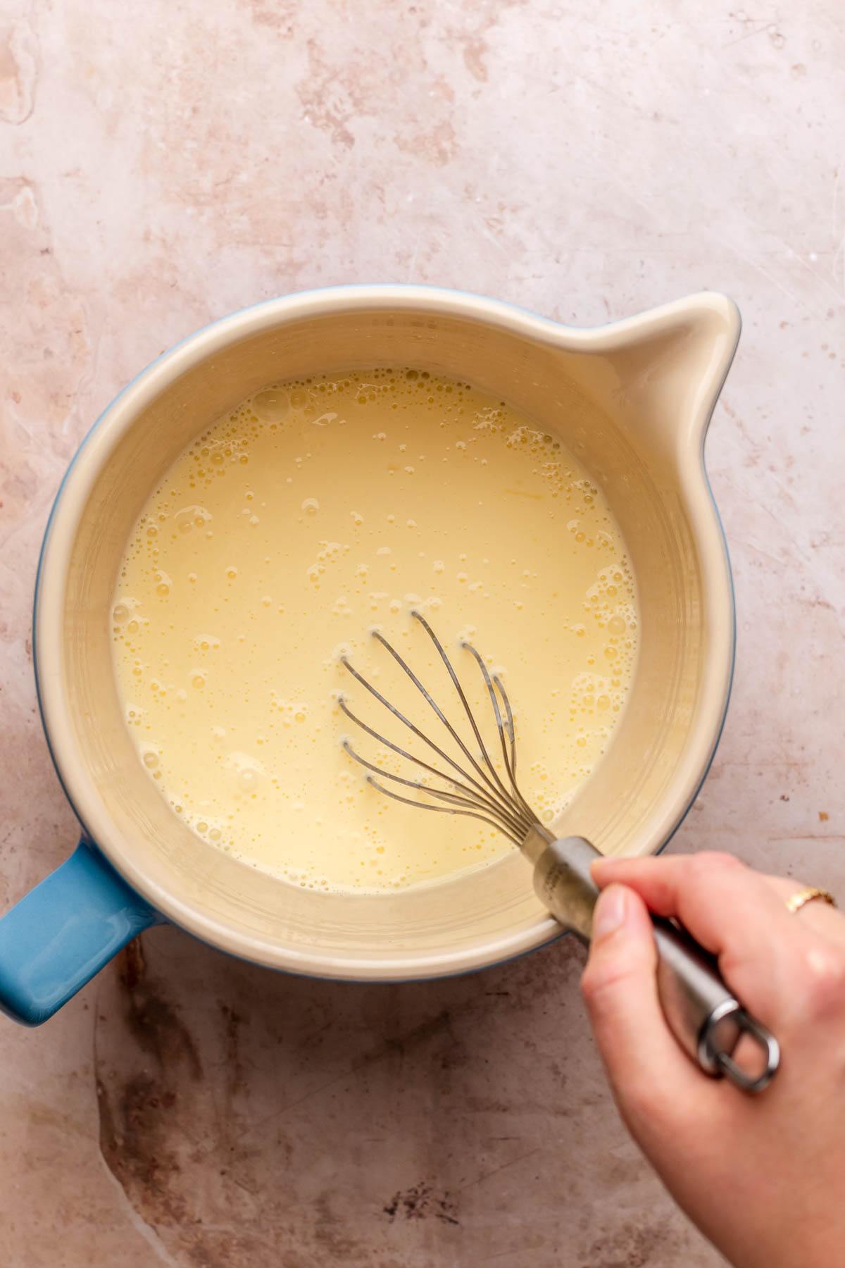 A bowl of egg custard with a whisk in it.