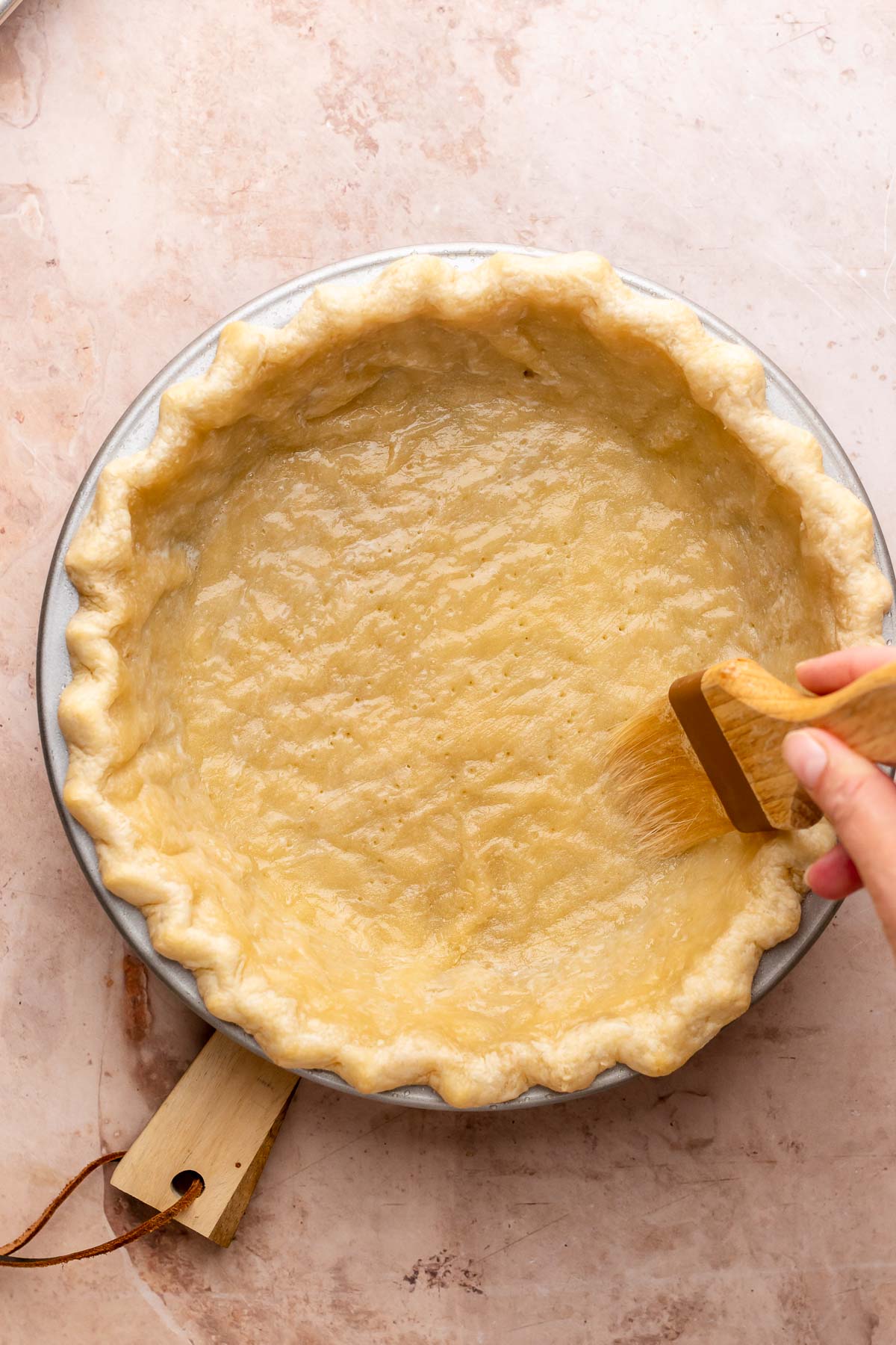 A hand brushes egg wash onto par-baked crust.