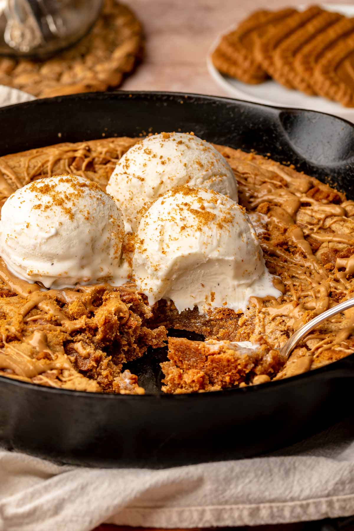 Skillet cookie with ice cream on top and spoons laying inside with pieces removed.