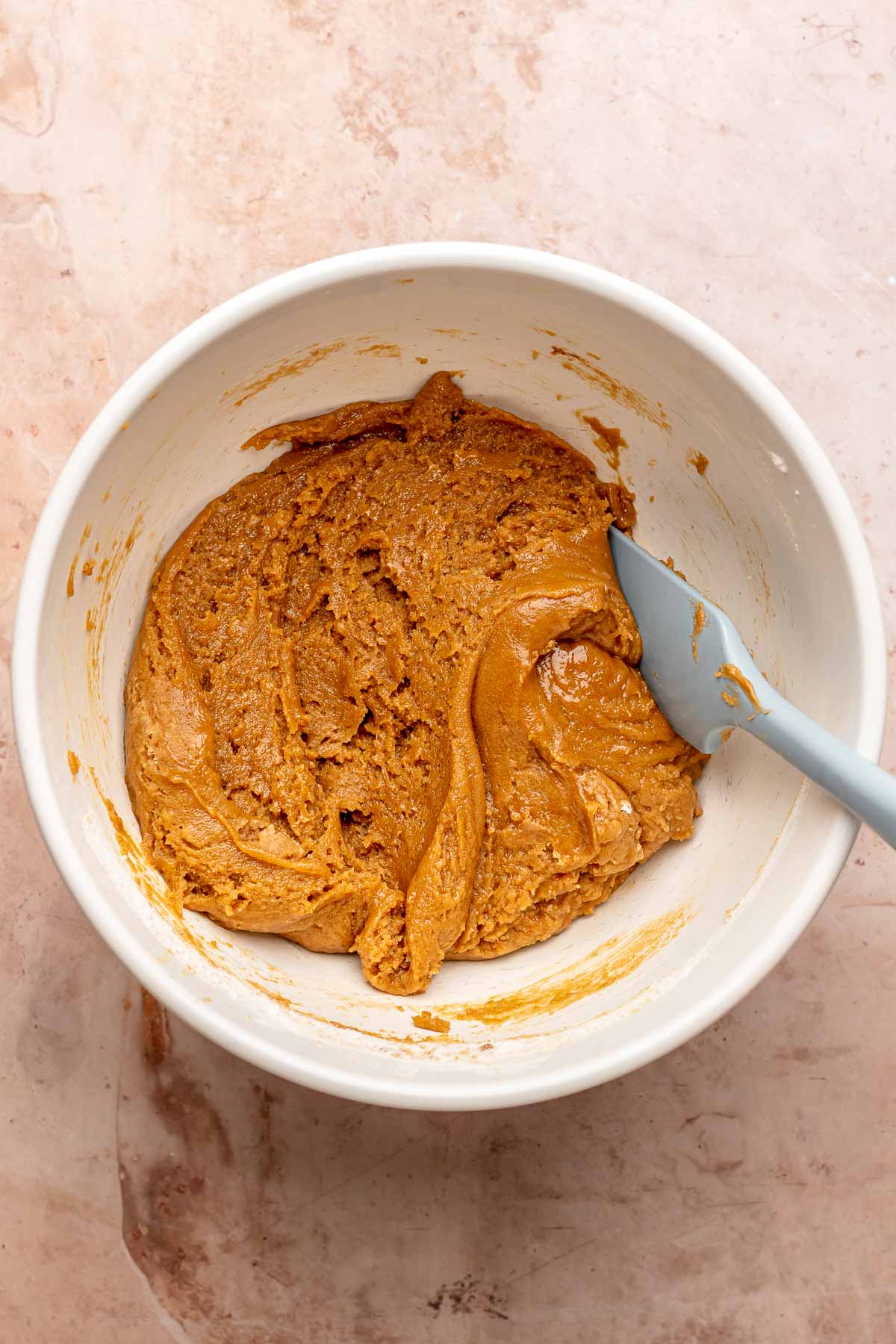 A rubber spatula mixes cookie butter batter in a bowl.